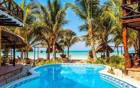 A pool area with a view of the beach, surrounded by palm trees and lounge chairs.