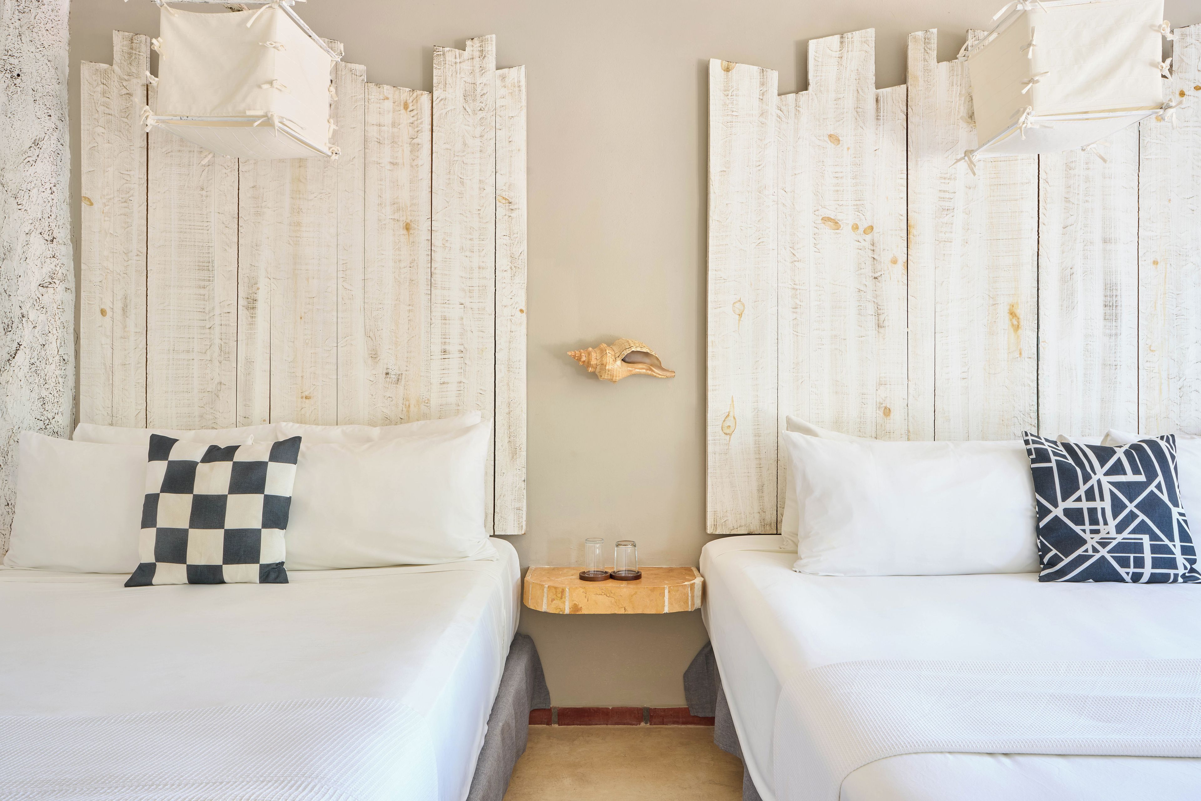 A hotel room with two beds, white bedding, a checkered pillow, a decorative shell, and a small wooden nightstand.