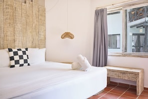 A hotel room with a bed, checkered pillow, a woven headboard, a small wall decoration, a window with curtains, and a bench. - Holbox Dream Beach Front Hotel  (Isla Holbox)