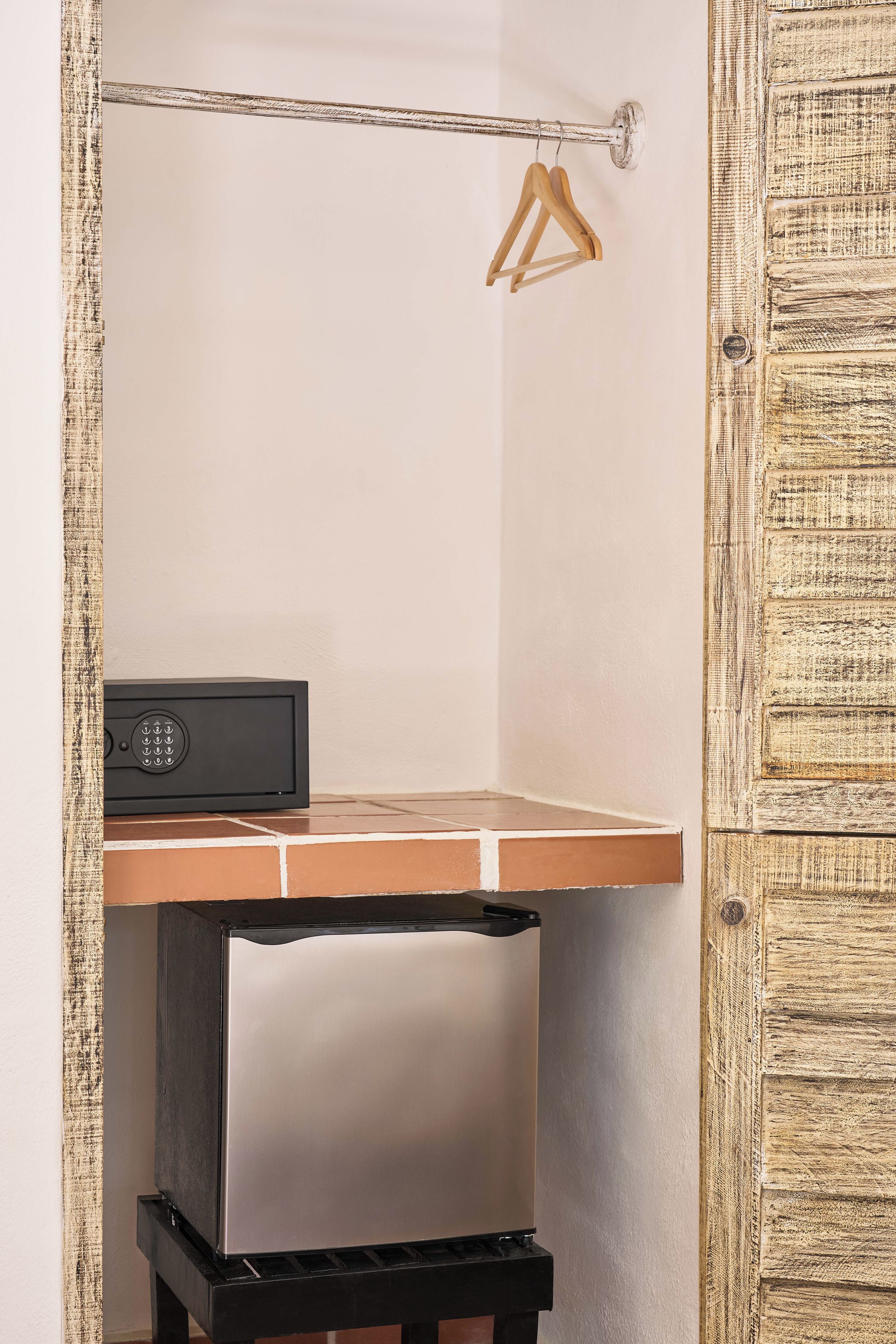 Quarto compacto com escrivaninha embutida, um pequeno alto-falante preto e um cabide de madeira na parede.