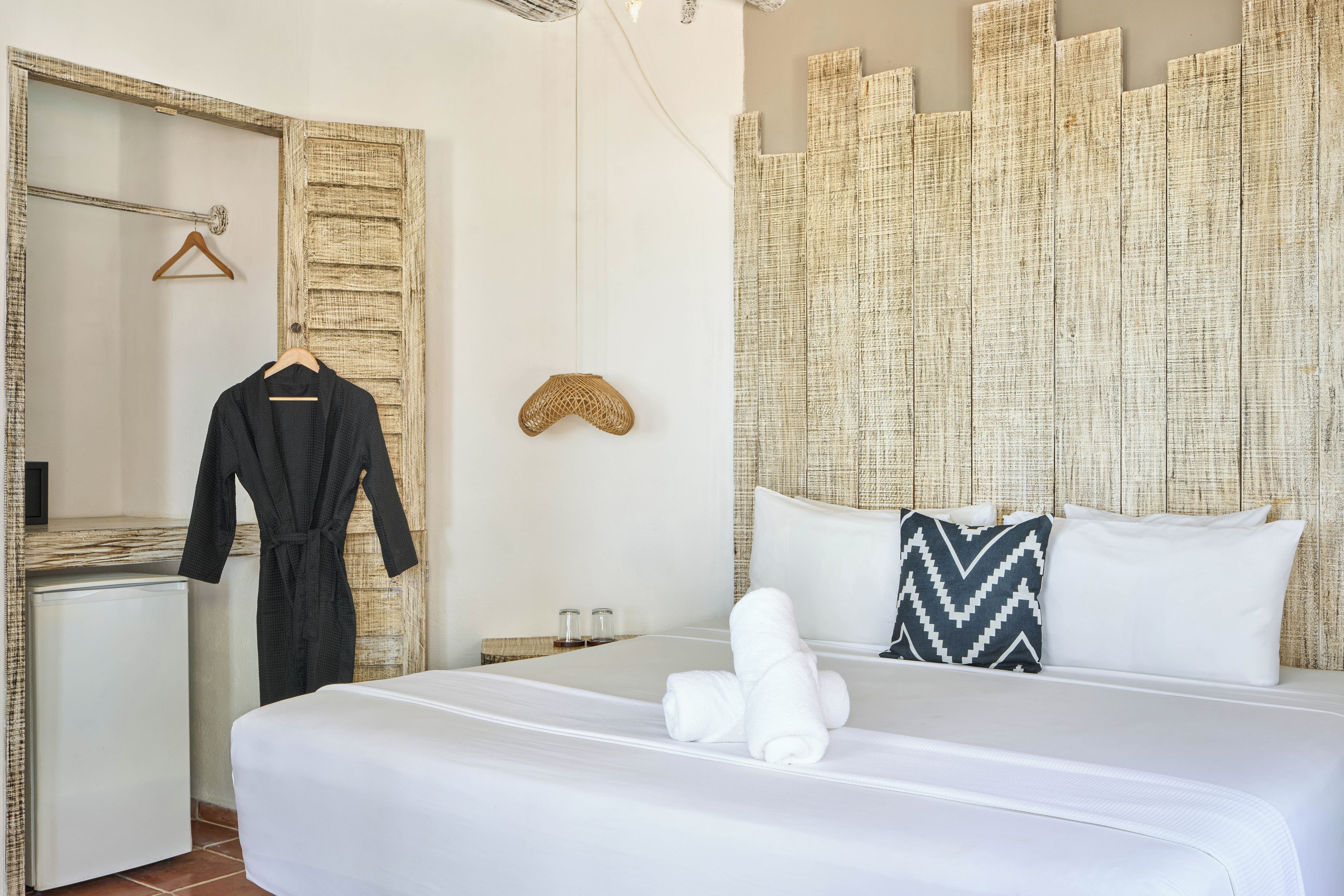 Habitación de hotel con cama, espejo, bata, toalla y pared con textura.