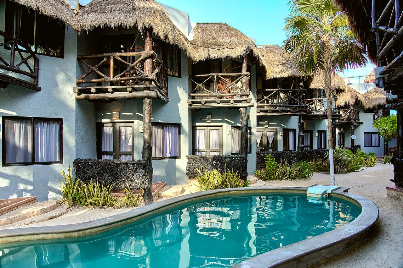 Un resort con edificios de techo de paja, piscina y exuberante jardinería tropical.