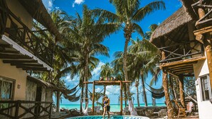 A pool area with a view of the ocean, surrounded by palm trees and thatched-roof structures. - Holbox Dream Beach Front Hotel  (Isla Holbox)