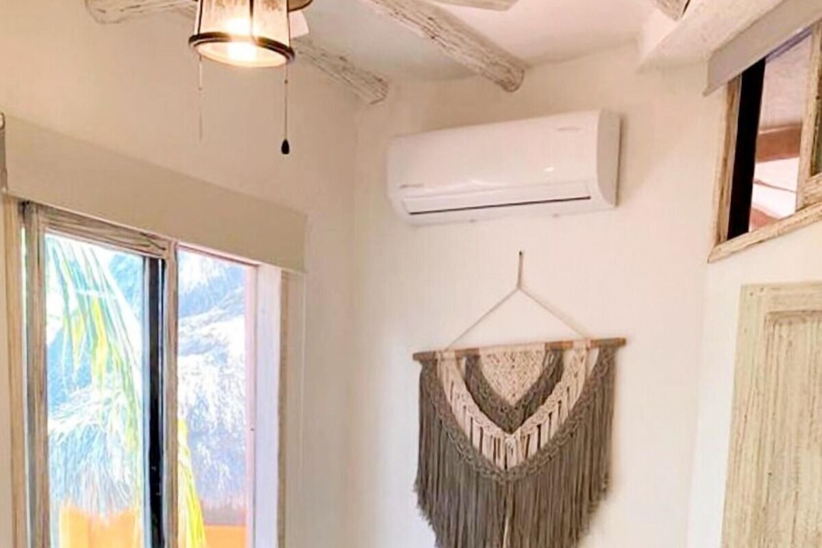 Una habitación con dos camas, un adorno de macramé en la pared y un equipo de aire acondicionado.