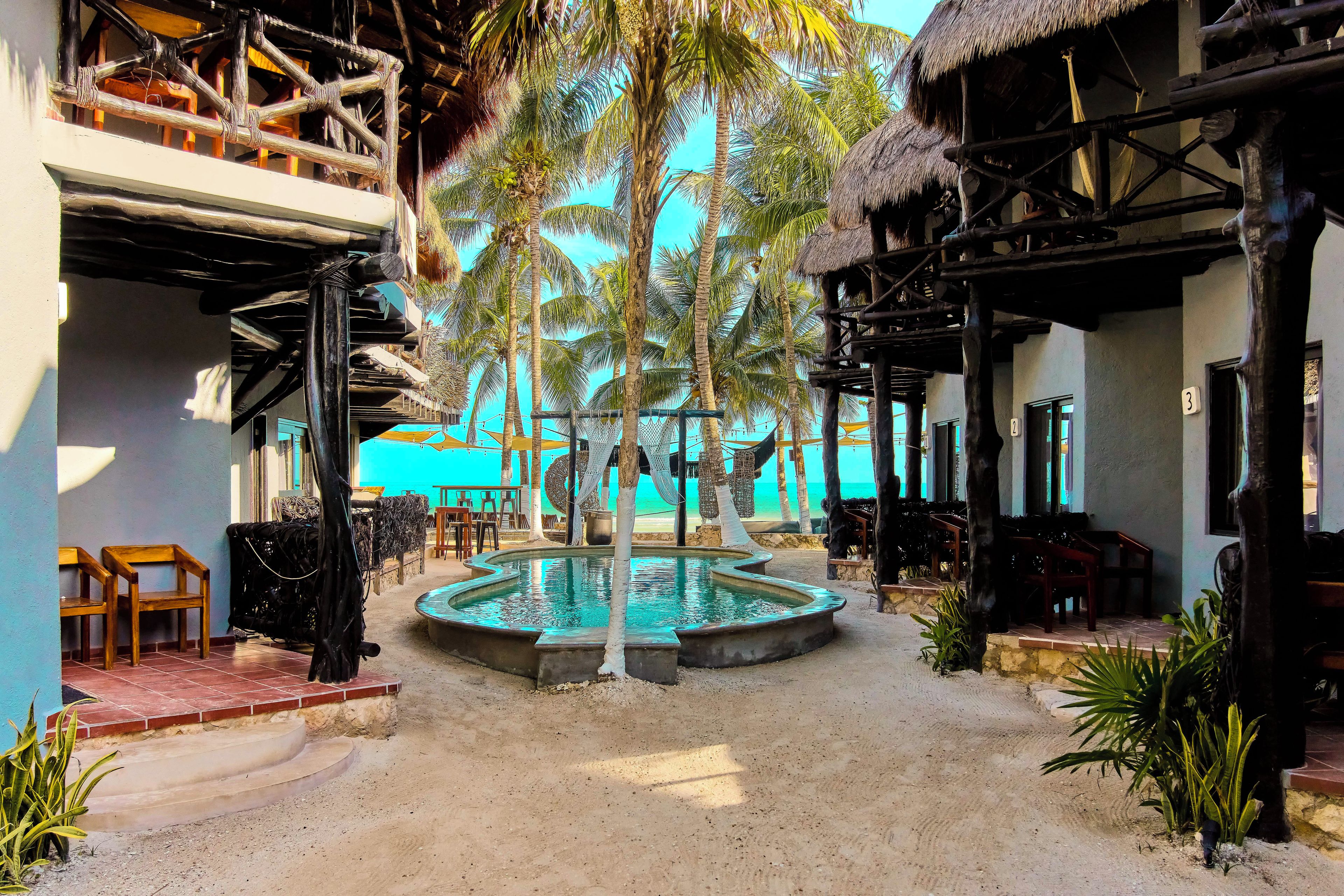 A resort with a pool, palm trees, and thatched-roof structures.