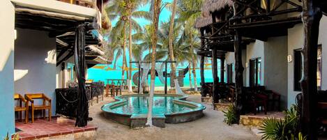 A resort with a pool, palm trees, and thatched-roof structures.