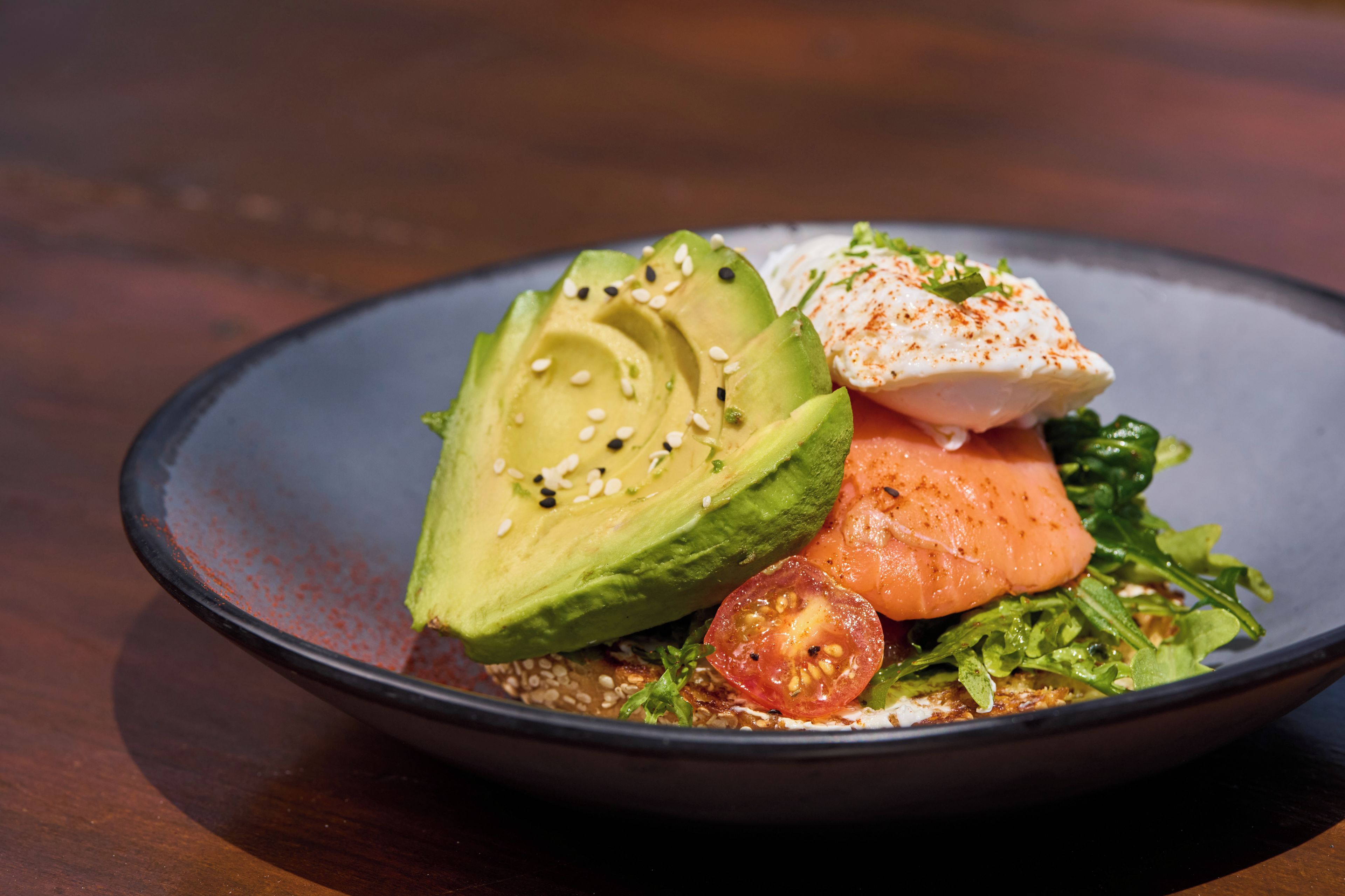Un tazón de comida con aguacate, salmón y vegetales verdes.