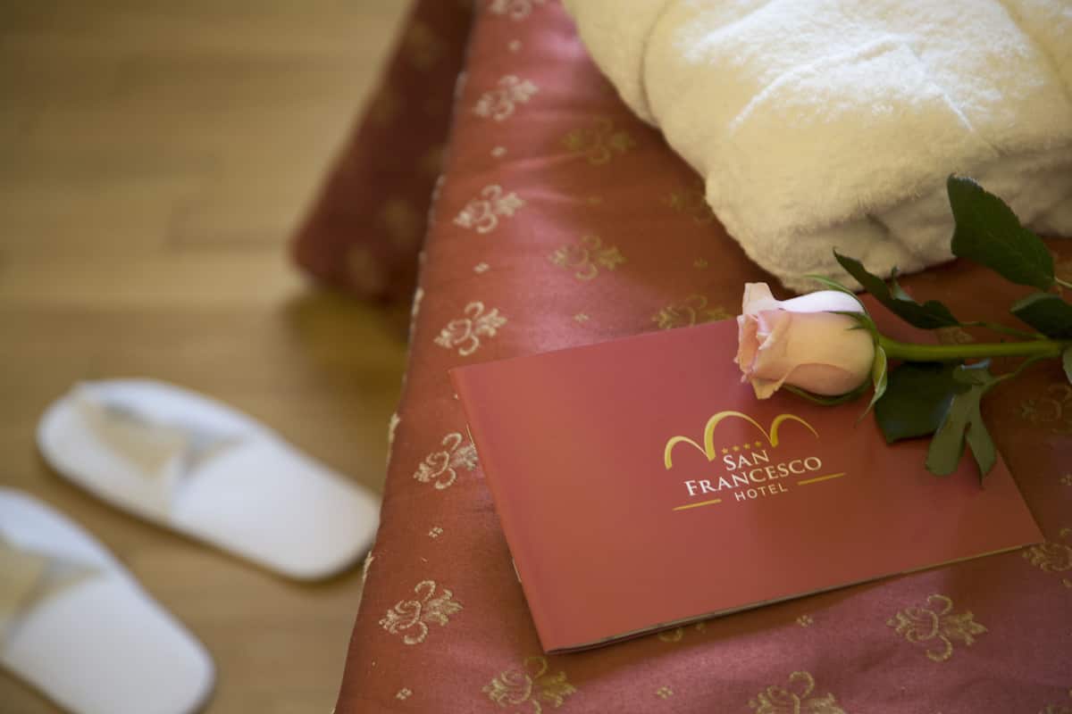 A hotel room with a bed, a rose, slippers, and a red card with hotel branding.