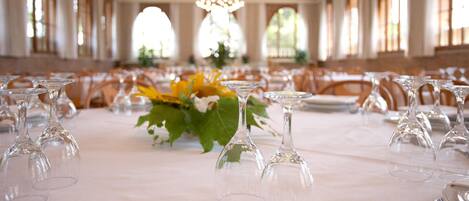 Un salón de banquetes con largas mesas dispuestas para un evento formal, destacando copas de cristal y centros de mesa florales.