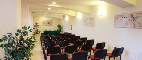 Sala de conferências com fileiras de cadeiras, uma mesa verde e obras de arte nas paredes.
