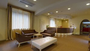 A hotel lobby with a reception desk, two sofas, a coffee table, and a large window with curtains. - San Francesco Hotel (Loreto)