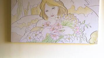 A wall-mounted artwork of a woman with flowers, a bed with a patterned headboard, and a plain wall.