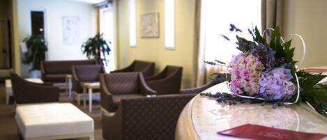 A hotel lobby with seating arrangements, a reception desk, and a decorative floral arrangement.