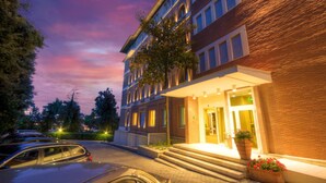 A multi-story hotel with a brick facade, a well-lit entrance, and a parking area with cars. - San Francesco Hotel (Loreto)