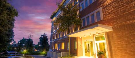 A multi-story hotel with a brick facade, a well-lit entrance, and a parking area with cars.