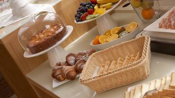 A buffet with a variety of food items including bread, pastries, fruits, and a covered cake.