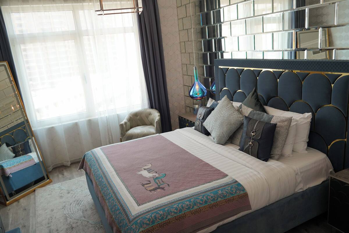 A bedroom with a large bed, a mirror, a chair, and a bedside table.