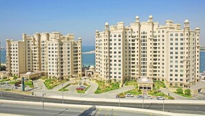 A high-rise residential building with multiple balconies, a landscaped courtyard, and a view of the sea.