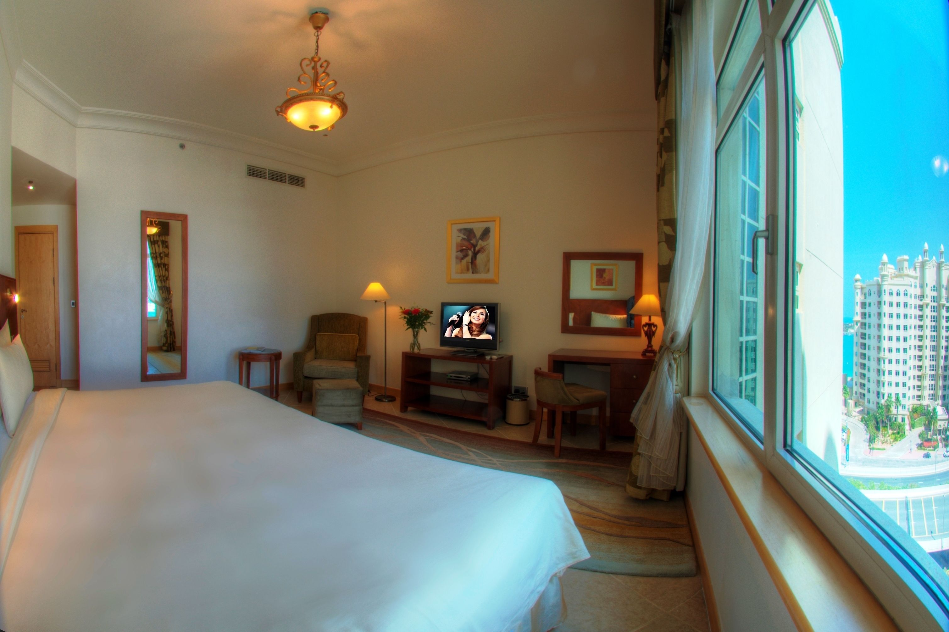 Une chambre d’hôtel avec un grand lit, une télévision, un bureau avec une lampe et une vue sur le paysage urbain par la fenêtre.