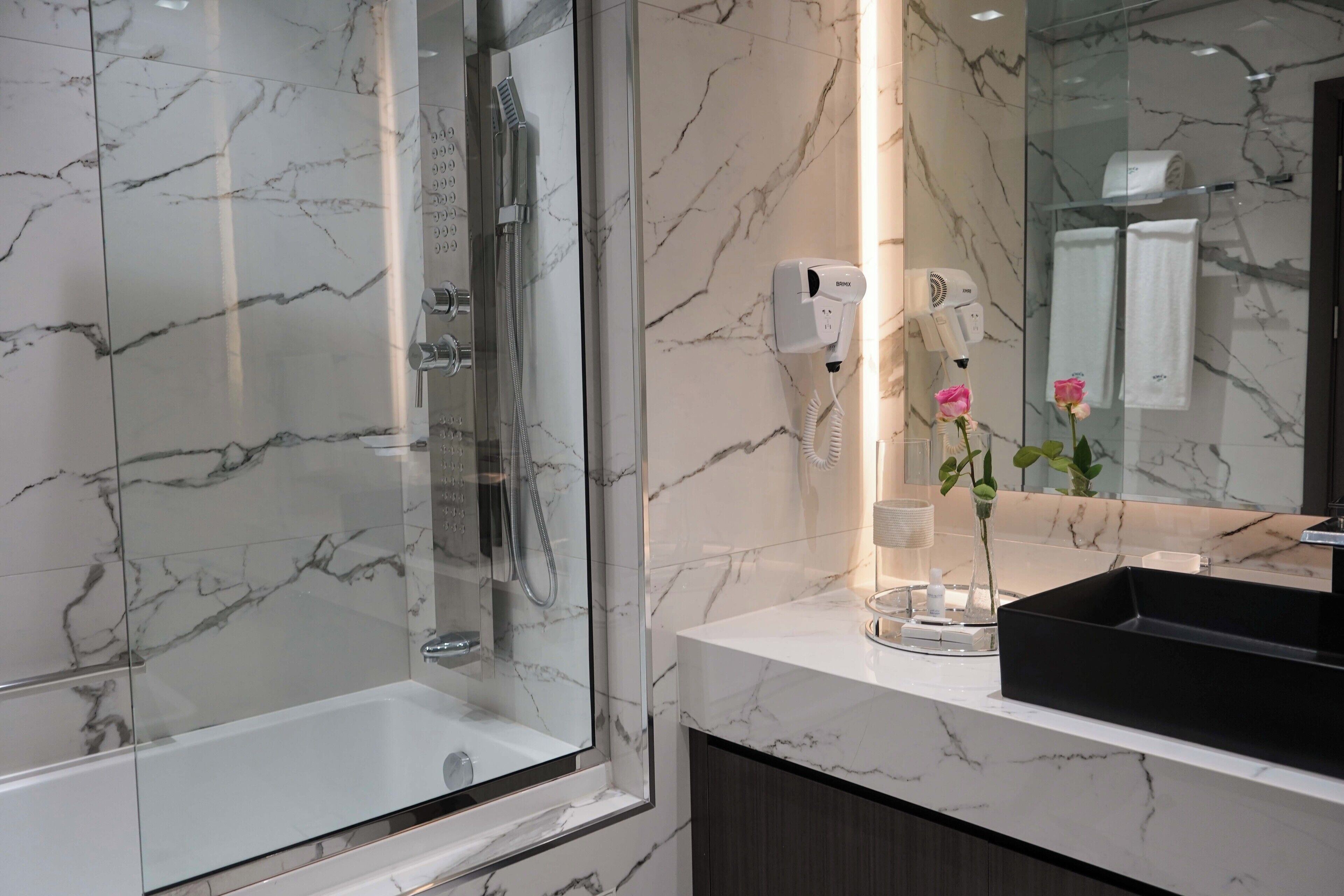 Un baño moderno con ducha de vidrio, lavamanos de mármol blanco y secador de pelo montado en la pared.