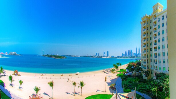 A beachfront hotel with a view of the ocean and a city skyline in the distance.
