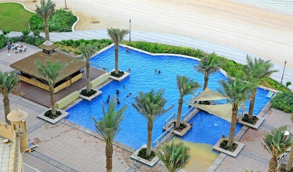A large outdoor swimming pool surrounded by palm trees and a small pavilion.