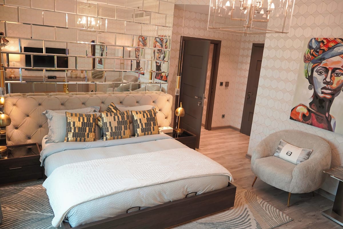 A modern bedroom with a large bed, a chair, a TV, and a wall with artwork.