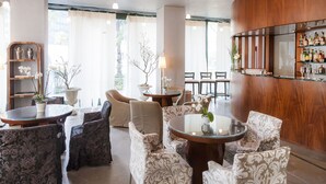 Een goed verlichte binnenruimte met meerdere zithoeken, waaronder ronde tafels en stoelen, en een bar met flessenkasten.
