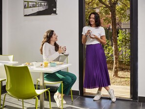 Two people dining indoors with a table, chairs, and a window with a view of greenery. - Aparthotel Adagio Access Paris Bastille (Paris)