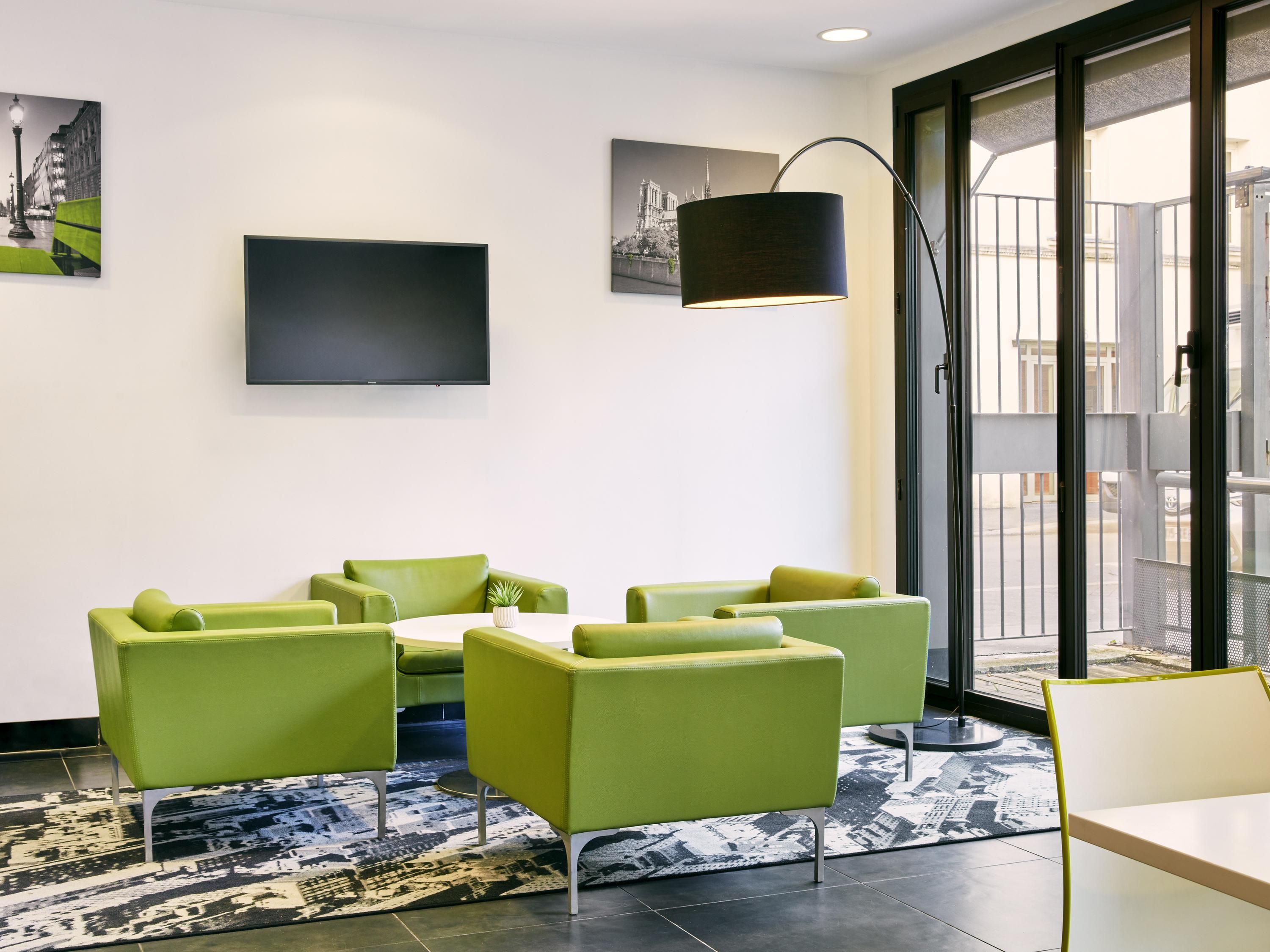 Un moderno vestíbulo de hotel con asientos verdes, un televisor de pantalla plana y obras de arte en las paredes.