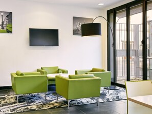 Un hall d’hôtel moderne avec des sièges verts, un téléviseur à écran plat et des œuvres d’art accrochées aux murs.