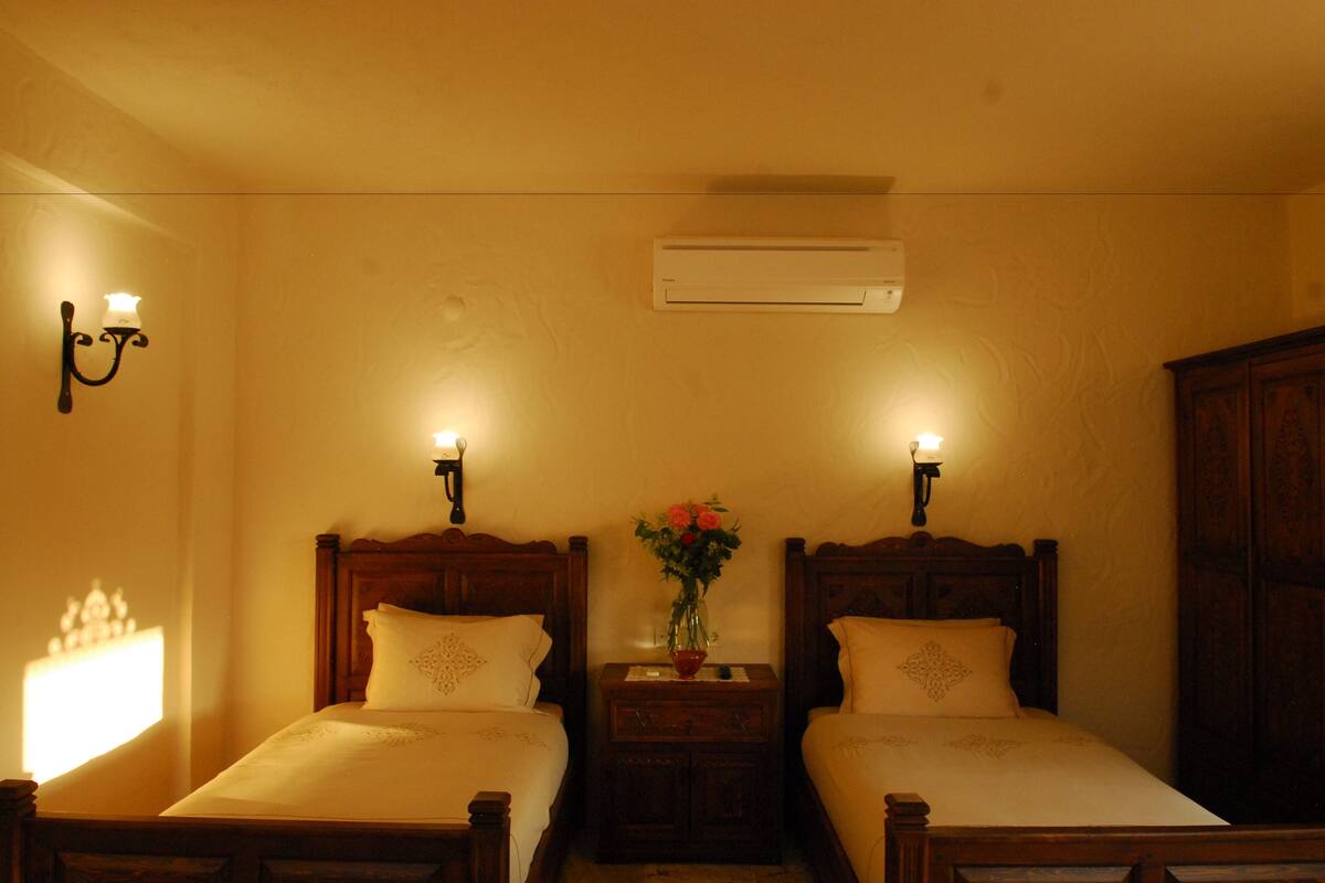 Habitación de hotel con dos camas, una mesita de noche con un florero y apliques de pared.