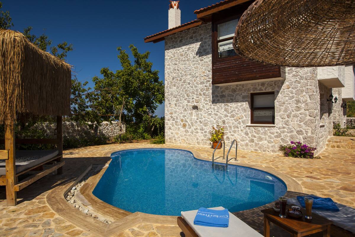 Un edificio de piedra con piscina, terraza de madera y estructura de techo de paja.