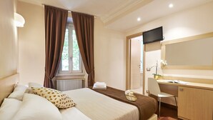 A hotel room with a bed, a desk, a chair, a television, and a window with curtains. - La Piccola Maison (Rome)