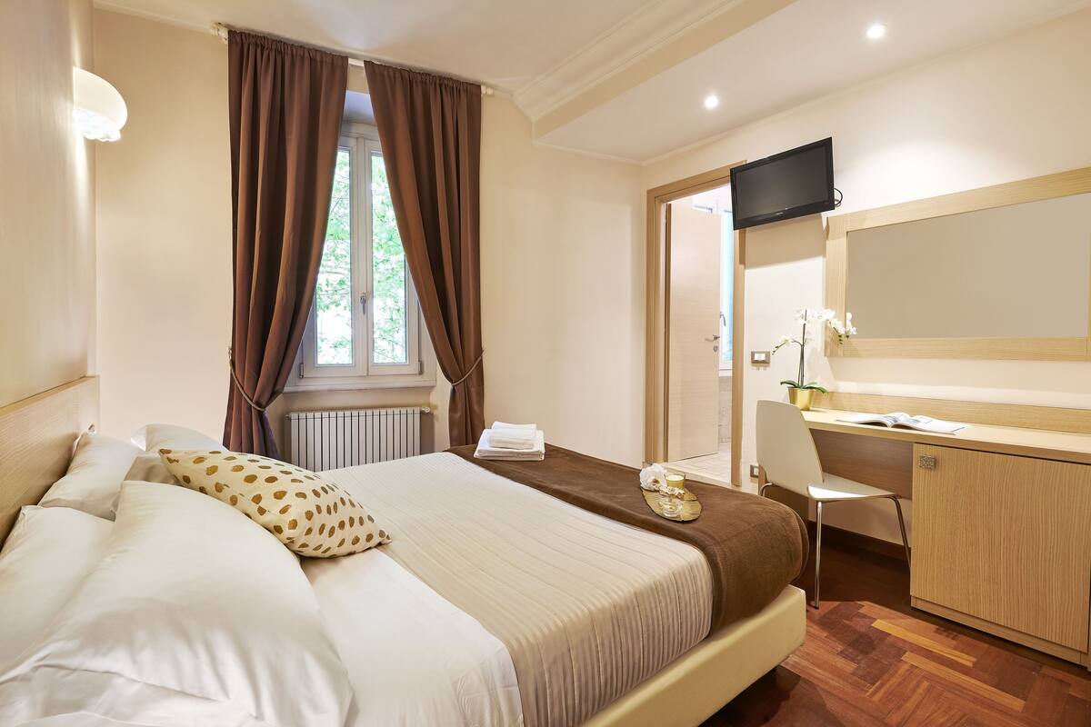 A hotel room with a bed, a desk, a chair, a television, and a window with curtains.