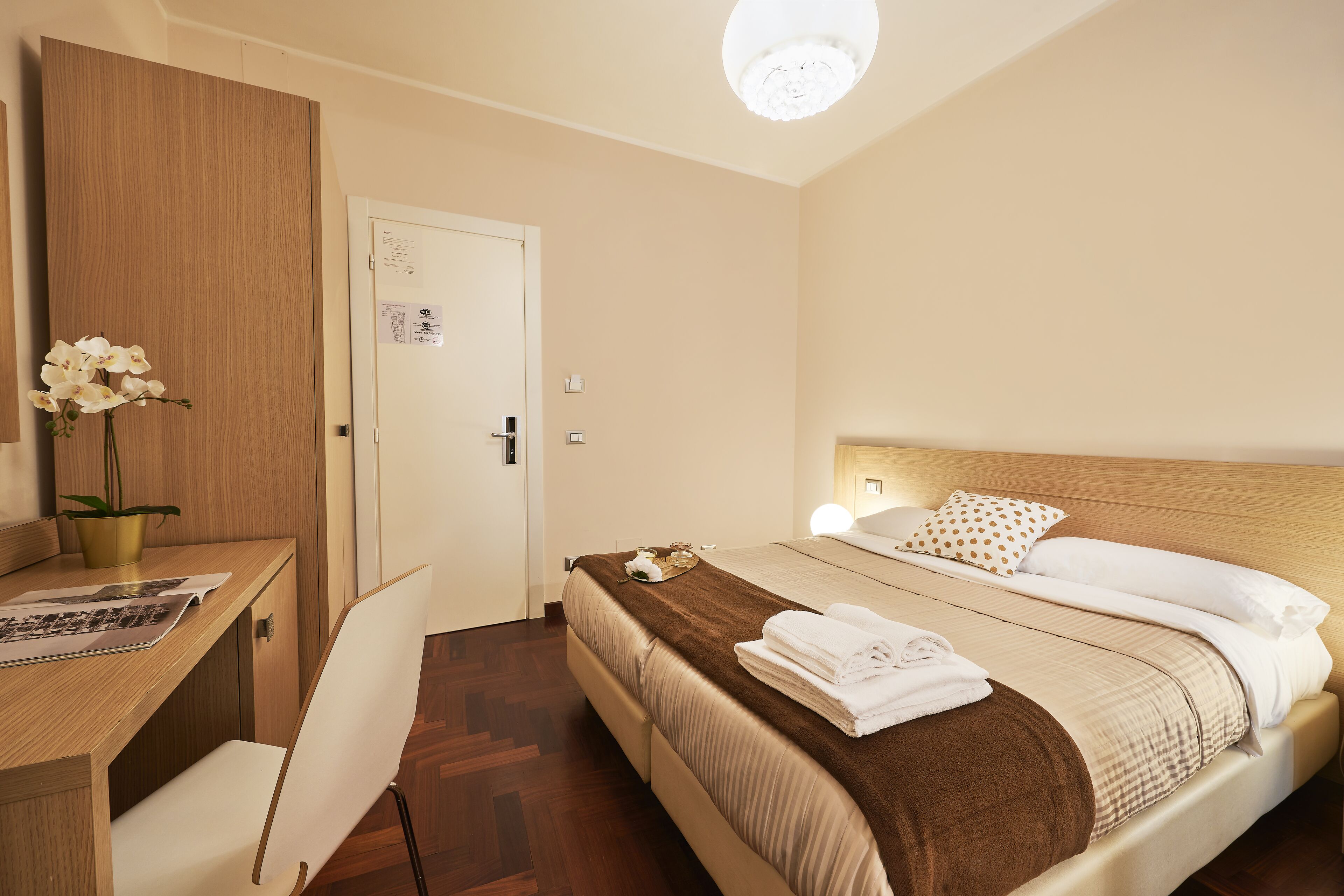 A neatly arranged bedroom with a bed, bedside table, chair, and a desk with a plant.