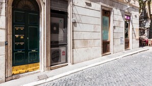 A building with a large arched entrance, a door with a security keypad, and a window with a metal grill. - La Piccola Maison (Rome)