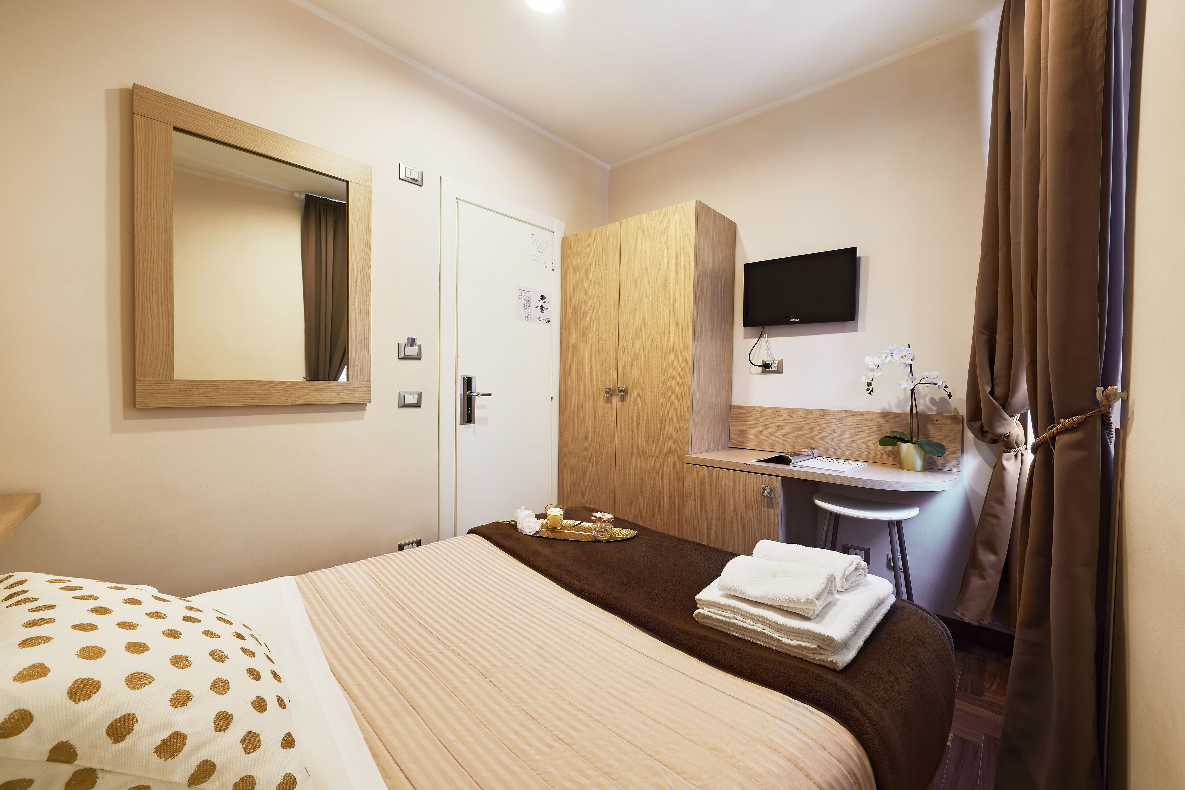 A hotel room with a bed, a desk with a chair, a TV, and a bathroom with a sink and mirror.
