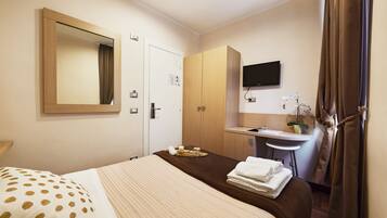 A hotel room with a bed, a desk with a chair, a TV, and a bathroom with a sink and mirror.