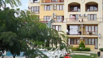 Un hotel de varios pisos con balcones, unidades de aire acondicionado y un área de piscina con sillas de descanso.