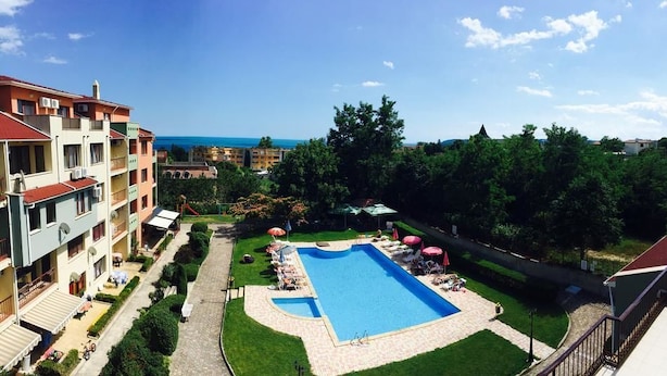 Una piscina rodeada de sillas de descanso y sombrillas, con vista al mar y edificios cercanos.