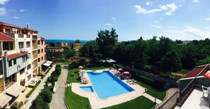 Una piscina rodeada de sillas de descanso y sombrillas, con vista al mar y edificios cercanos.