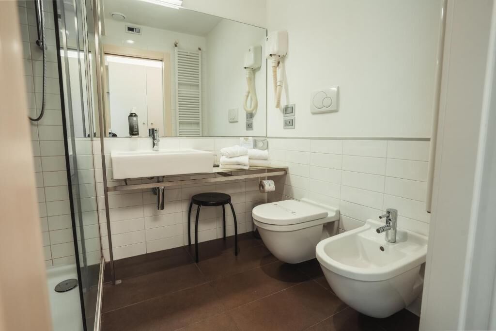 A modern bathroom with a glass shower enclosure, a white sink, a bidet, and a mirror.