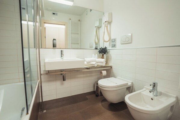 Une salle de bain moderne avec une douche à parois de verre, un lavabo blanc, un bidet et un meuble-lavabo sur pied.