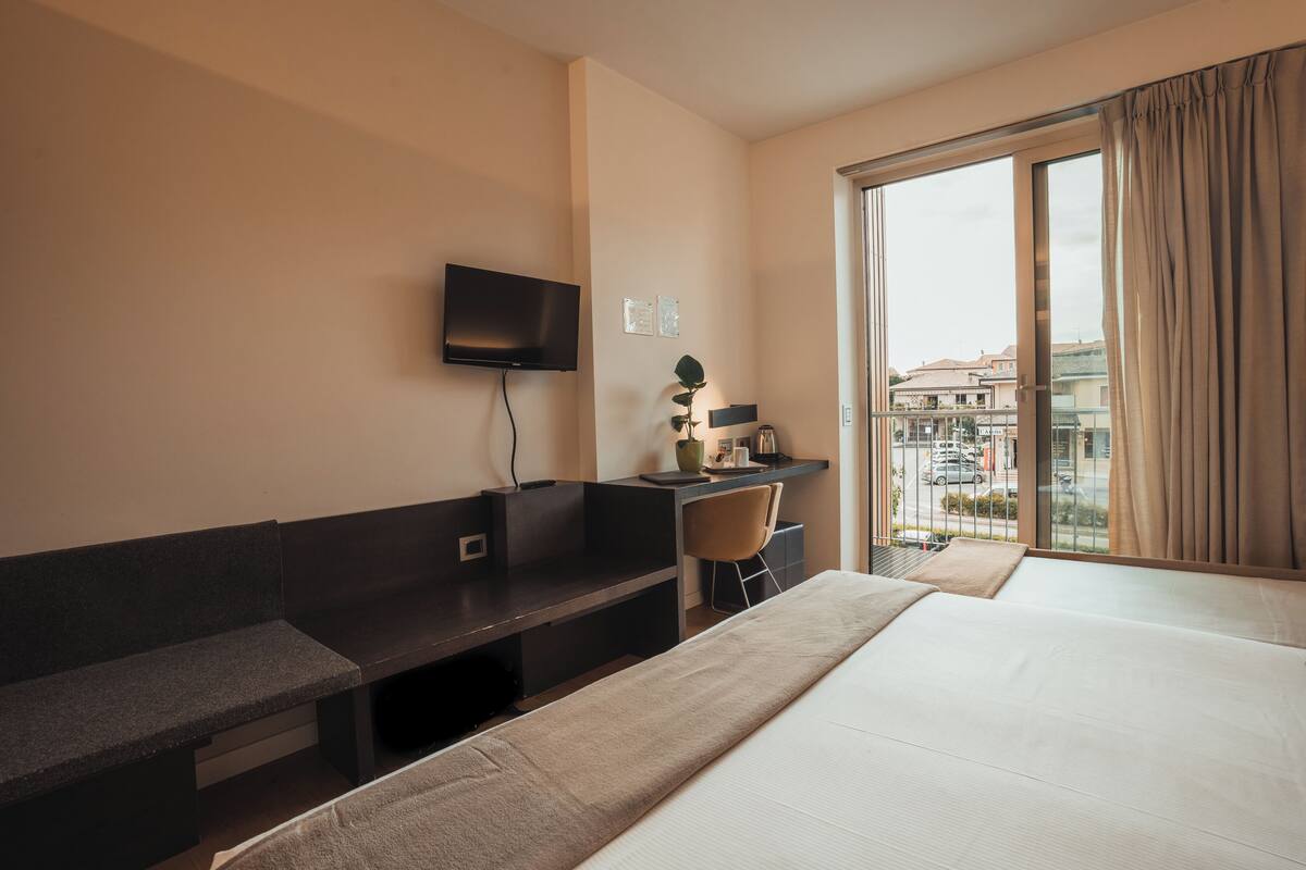 A hotel room with a bed, a desk, a chair, a television, and a window with curtains.