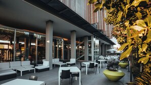 An outdoor seating area with white tables and chairs, large planters, and a modern architectural design with large windows and columns.