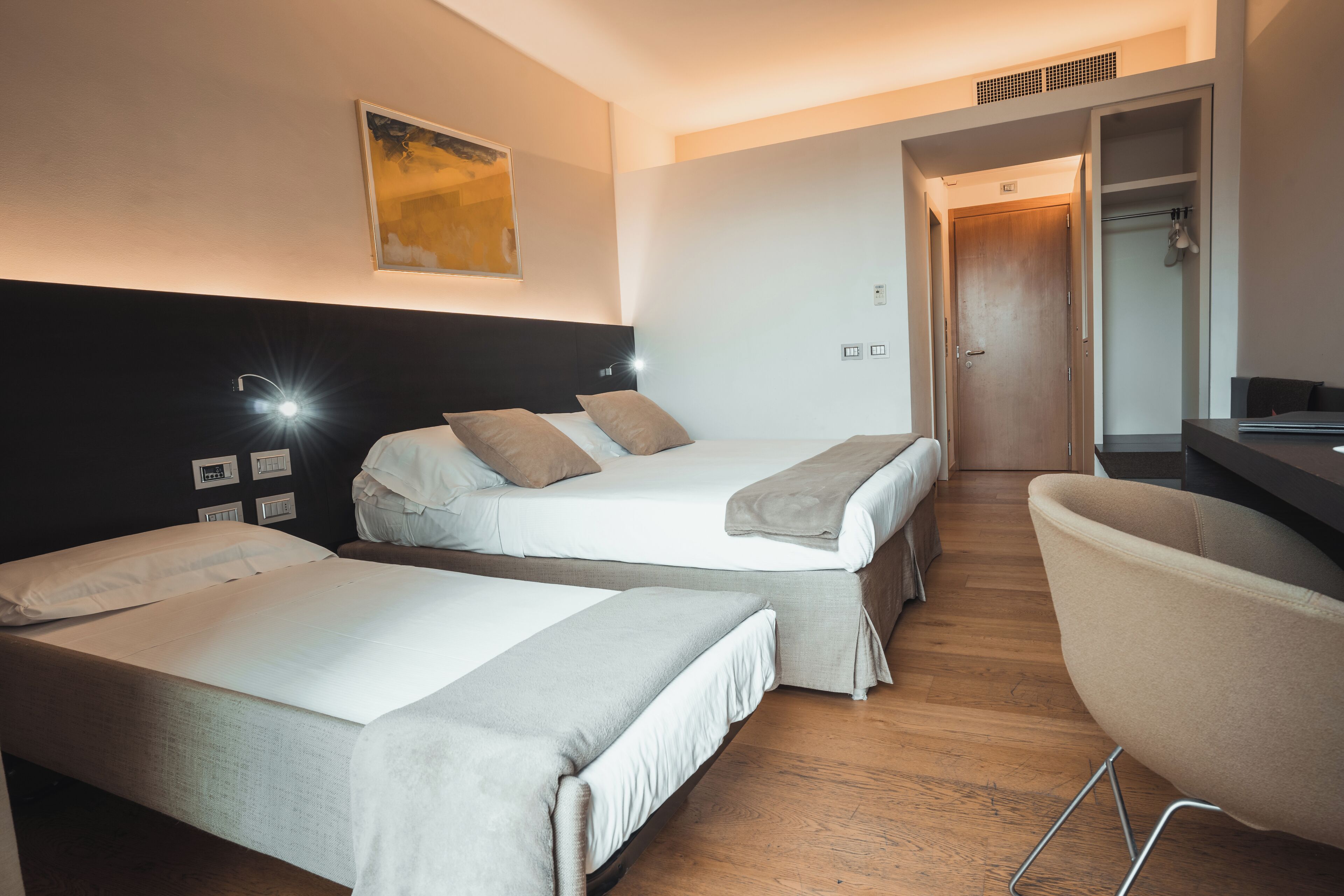 A hotel room with two single beds, a desk, and a chair.