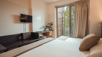 A hotel room with a bed, a desk, a chair, a TV, and a window with curtains.