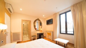 A hotel room with a bed, a bench, a fireplace, a mirror, a television, and a window with curtains. - Hotel Globo Suite (Sanremo)