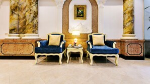 Eine Lobby mit zwei blauen Sesseln, einem kleinen Tisch mit Lampe und einem gerahmten Bild an der Wand.